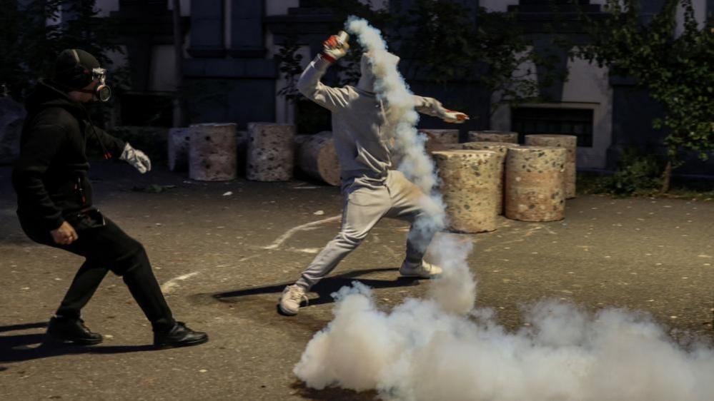 A protester throws a tear gas cartridge back towards police